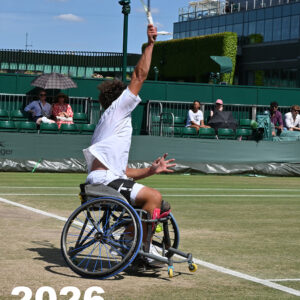 Shows a Wheelchair tennis player about to hit the tennis ball in a serve