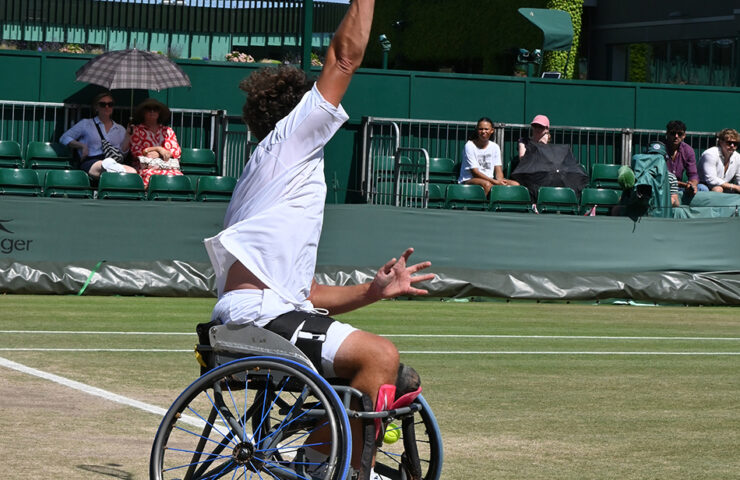 Shows a Wheelchair tennis player about to hit the tennis ball in a serve